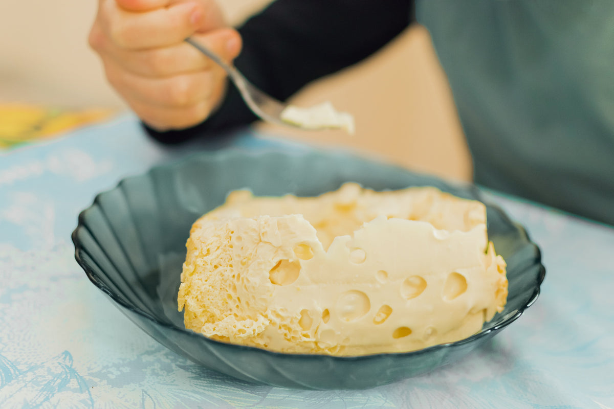 boy of European appearance sits at the table and has breakfast, he eats dairy products with a fork and makes emotions. Food concept 